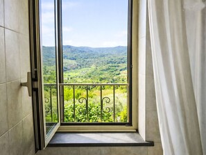 A window with a view of a green landscape, a metal balcony railing, and a white curtain. - Beautiful apartment for 4 guests with TV, patio and panoramic view (Collazzone)