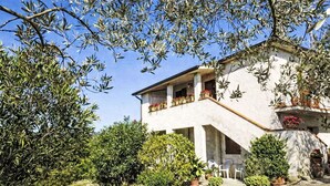 Ein zweistöckiges Haus mit Balkon, umgeben von viel Grün und Topfpflanzen.