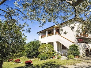 A two-story house with a balcony, surrounded by greenery and potted plants. - Beautiful apartment for 4 guests with TV, patio and panoramic view (Collazzone)