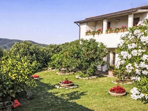A two-story building with a garden in front, surrounded by greenery and hills. - Beautiful apartment for 4 guests with TV, patio and panoramic view (Collazzone)