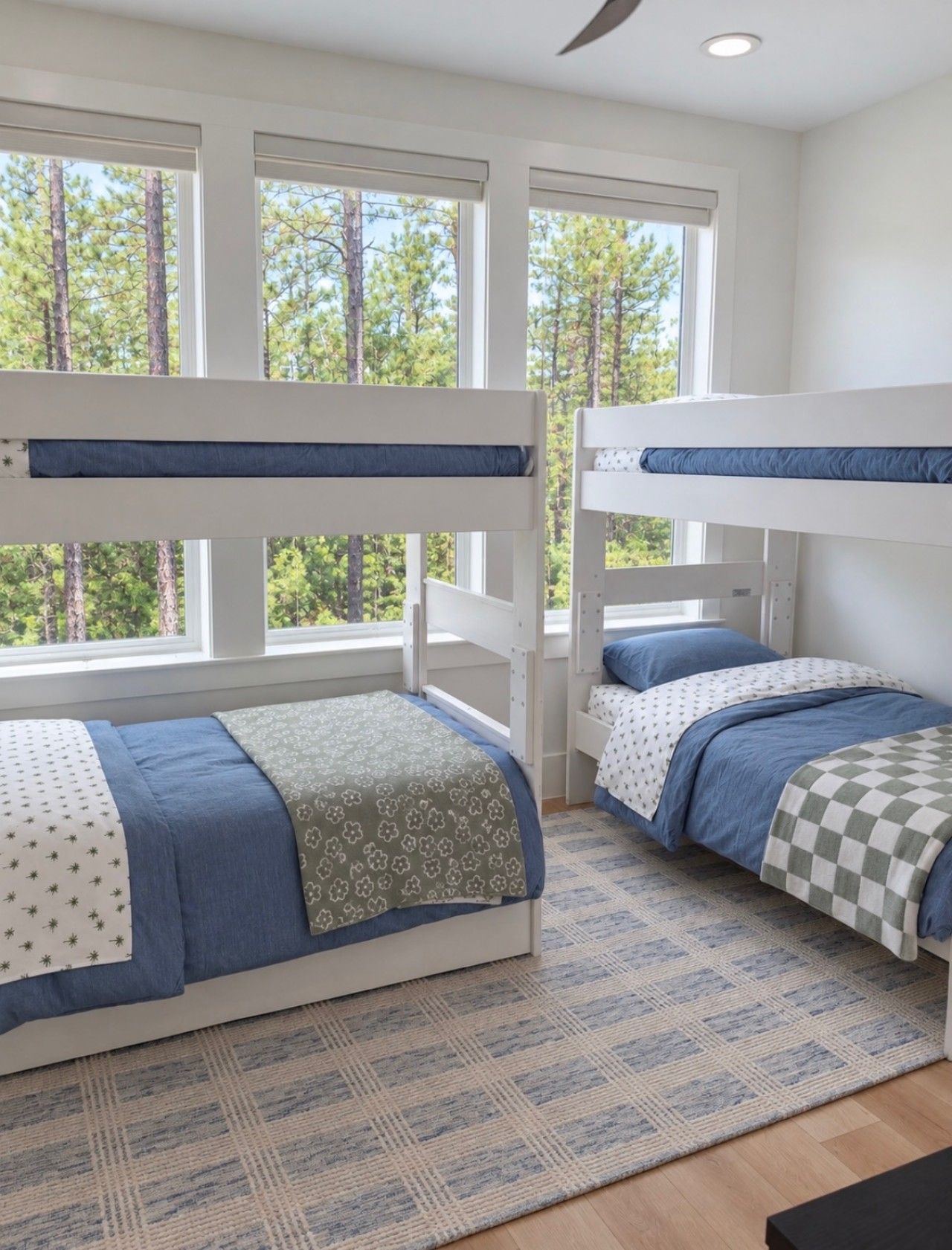 A room with bunk beds, a patterned rug, and a view of trees through large windows.