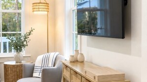 A modern living room with a flat-screen TV mounted on the wall, a grey armchair, a wooden console table, wicker baskets, and a floor lamp. - Escape to Paradise along the Emerald Coast (Rosemary Beach)
