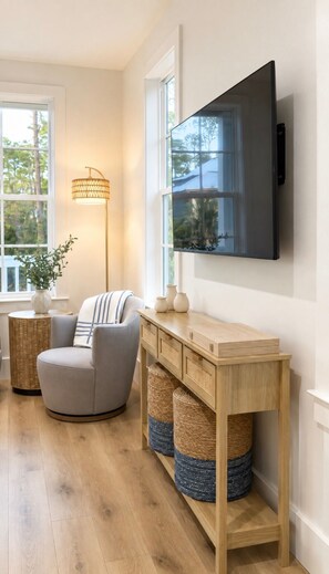 A modern living room with a flat-screen TV mounted on the wall, a grey armchair, a wooden console table, wicker baskets, and a floor lamp. - Escape to Paradise along the Emerald Coast (Rosemary Beach)