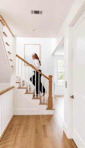 Un escalier avec des marches en bois et une rampe blanche, menant à une pièce où un tableau encadré est accroché au mur.