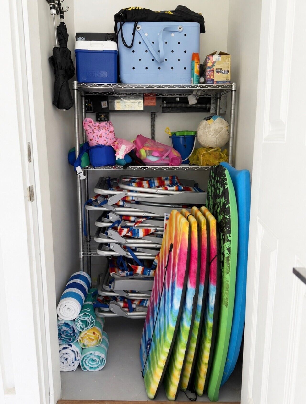 A storage unit with shelves holding various items including a blue cooler, a polka-dotted bag, and several colorful umbrellas.