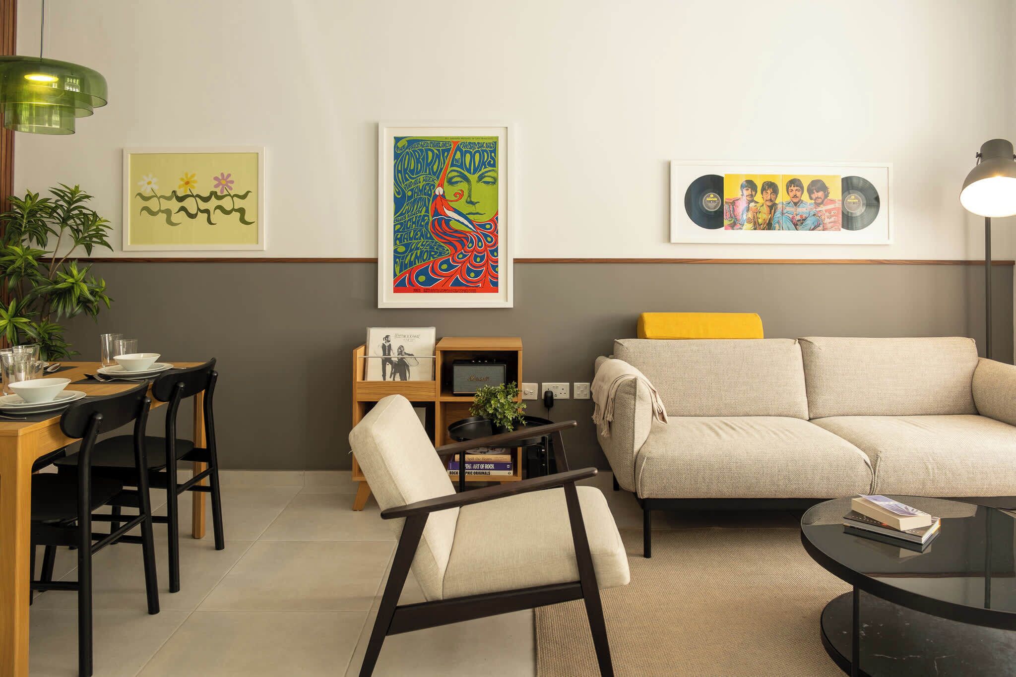 Ein modernes Wohnzimmer mit einer Couch, einem Esstisch mit Stühlen und einem Couchtisch. An der Wand hängen gerahmte Kunstwerke und auf dem Tisch steht eine Pflanze.