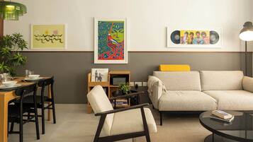 Ein modernes Wohnzimmer mit einer Couch, einem Esstisch mit Stühlen und einem Couchtisch. An der Wand hängen gerahmte Kunstwerke und auf dem Tisch steht eine Pflanze.