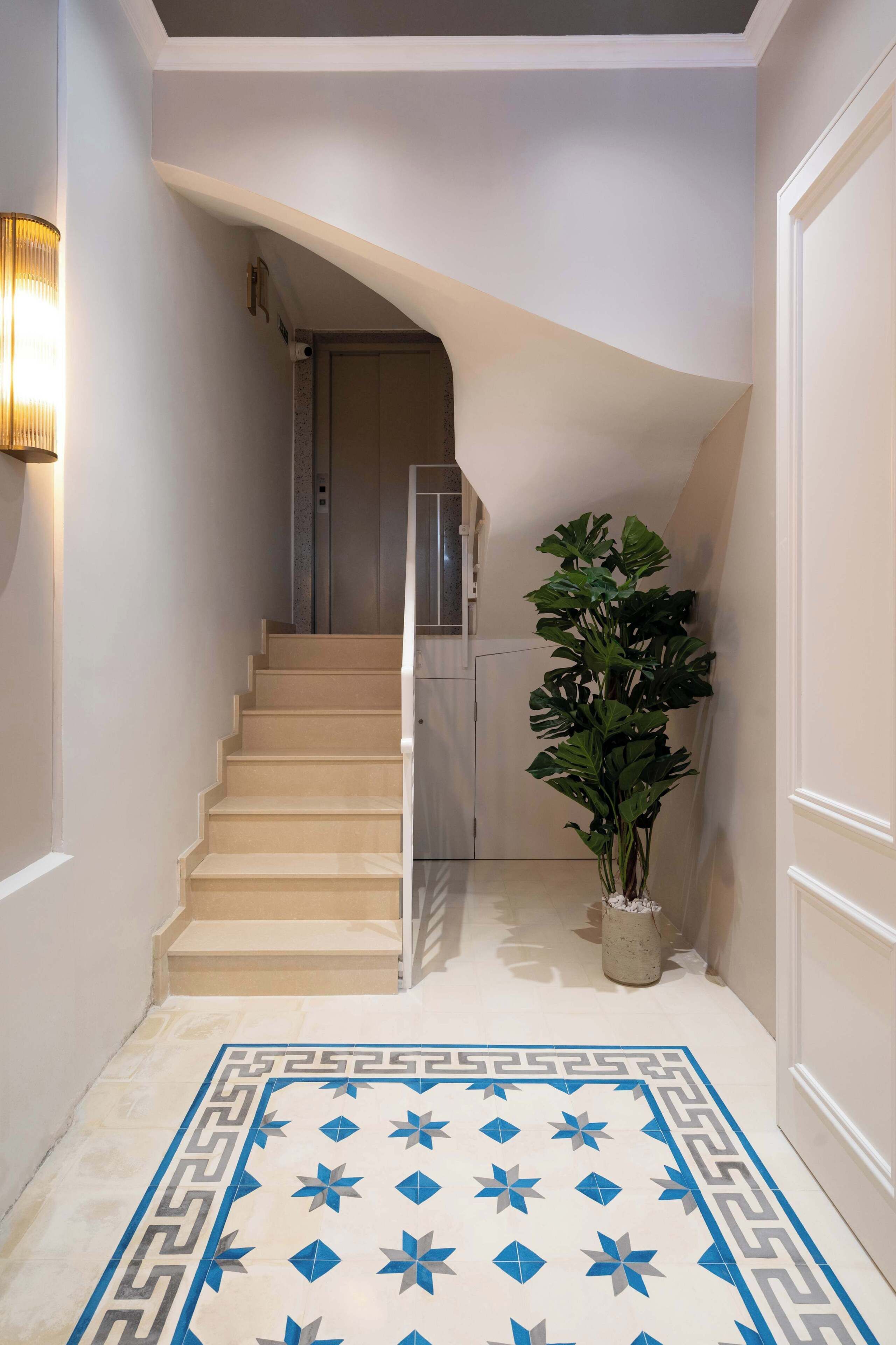 Eine Treppe mit einem geometrisch gemusterten Teppich, einer Topfpflanze und einer Wandleuchte.
