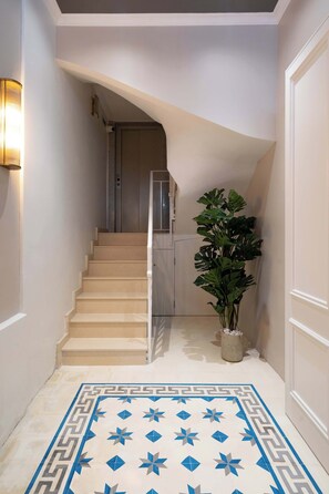 Eine Treppe mit einem geometrisch gemusterten Teppich, einer Topfpflanze und einer Wandleuchte.