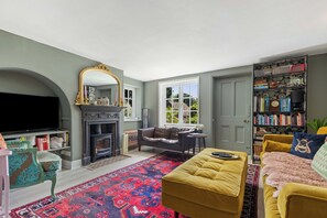 Ein Wohnzimmer mit Kamin, Sofa, Hocker und Bücherregal.