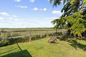 A grassy outdoor area with a wooden fence, a wooden chair, and a tree. - Beautiful Cottage near Goodwood Estate (East Lavant)