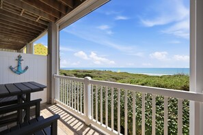 Ein überdachter Außenbereich mit Holzdeck, weißer Geländer und Blick auf Strand und Meer.