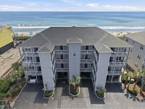 Um hotel com vários andares, entrada central, varandas e vista para a praia.