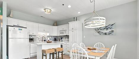 A modern kitchen with white cabinetry, a central island with stools, and a dining table set for six.