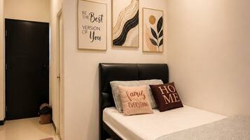 Un dormitorio con una cama, una pared con tres obras de arte enmarcadas, una puerta negra y un cesto de basura pequeño.