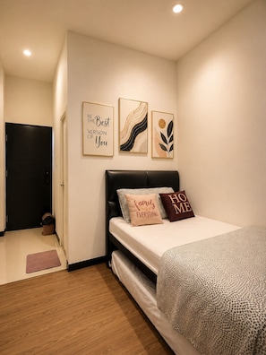 A bedroom with a bed, a wall with three framed artworks, a black door, and a small trash bin.