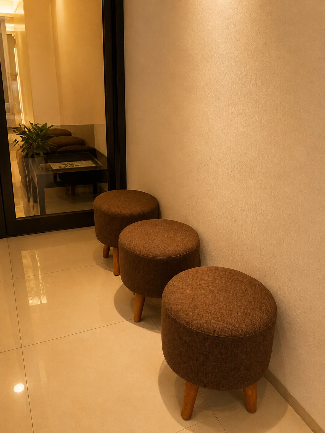 Two round ottomans with wooden legs against a wall in a room with a reflective floor.