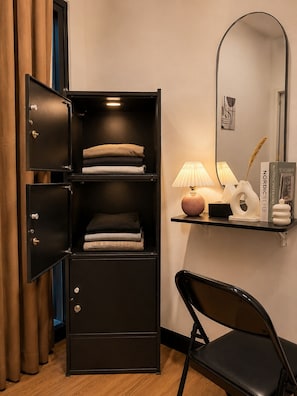 A room with a black metal cabinet with drawers, a desk with a lamp, and a chair.