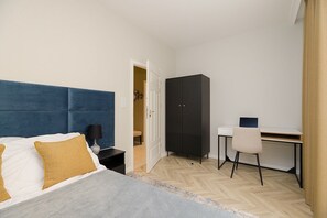 Ein Schlafzimmer mit Bett, Nachttisch, Schreibtisch, Stuhl, Kleiderschrank und einer Tür zu einem anderen Raum.