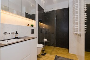 Moderni kylpyhuone, jossa on lasiseinällä varustettu suihku, wc ja pesuallas marmoritasolla.