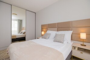 Moderni hotellihuone, jossa on suuri sänky, yöpöytä lampun kanssa, peili ja näkymä huoneeseen liukuoven kautta.