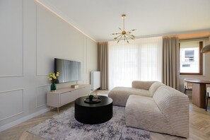 A modern living room with a sofa, a coffee table, a TV, and a chandelier. - Holzera 6 Apartament (Warszawa)