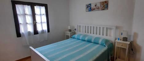 A bedroom with a single bed, a nightstand, a bedside table, a window with curtains, and a wall-mounted picture.