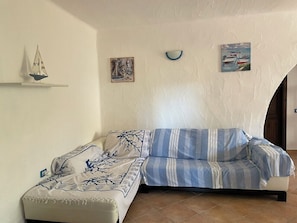 Ein Zimmer mit einer Couch, einem kleinen Tisch und einem an der Wand befestigten Regal mit einem Modellsegelboot und zwei Bildern.
