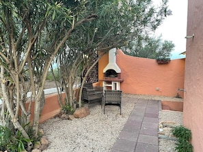 Eine Außenpatio-Terrasse mit Grill, Sitzgelegenheiten und einem kleinen Garten.
