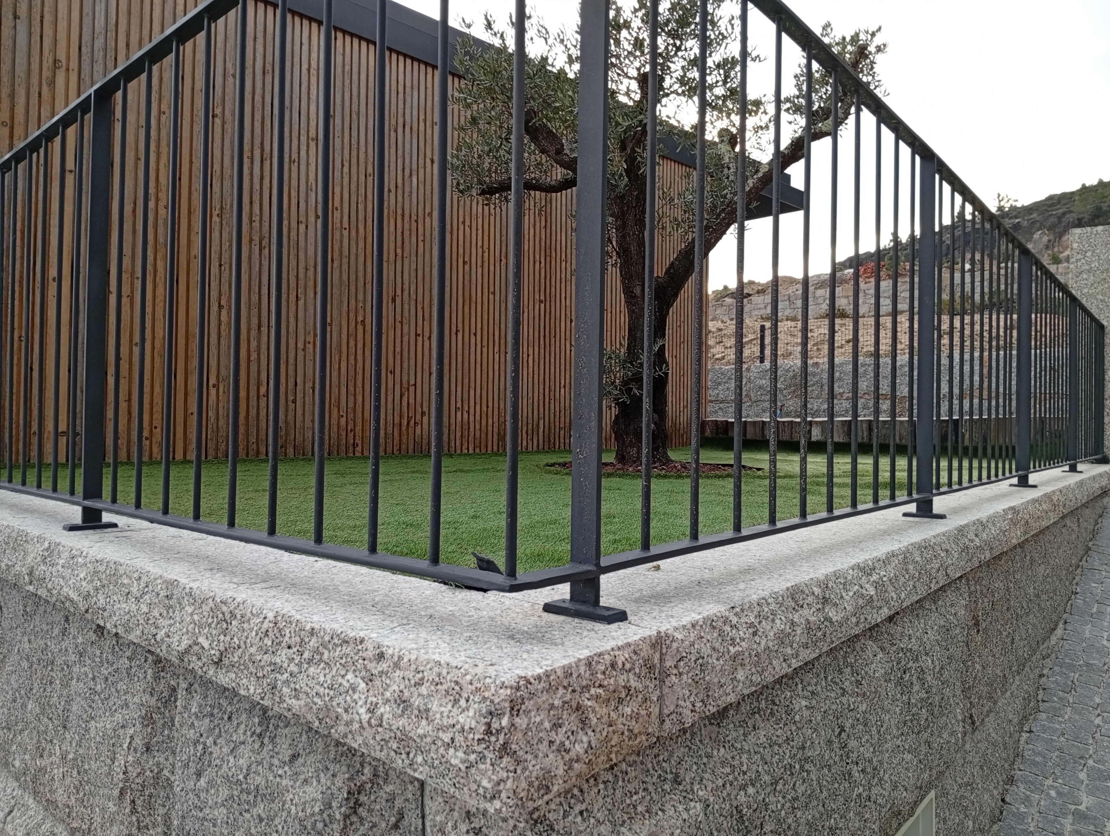 A stone wall with a metal fence in front of a wooden fence and a tree.