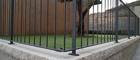 A stone wall with a metal fence in front of a wooden fence and a tree.