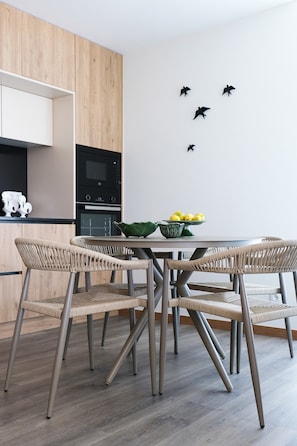 A modern kitchen with a dining area, featuring a wooden cabinet, a built-in oven, a microwave, and a table with chairs. - Casa Roca do Touro: Mountain View, Wi-Fi & Air Conditioning (Cabril)