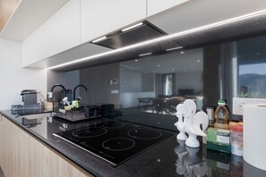 Eine moderne Küche mit einem schwarzen Induktionskochfeld, Edelstahlgeräten und einer Glasrückwand.