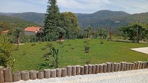 A grassy area with a wooden fence, a paved walkway, and a view of distant hills. - Casa Roca do Touro: Mountain View, Wi-Fi & Air Conditioning (Cabril)