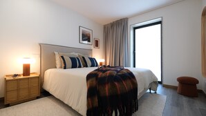 A modern bedroom with a large bed, bedside lamps, a wooden nightstand, a rug, and a window with curtains. - Casa Roca do Touro: Mountain View, Wi-Fi & Air Conditioning (Cabril)