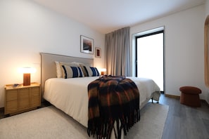 A modern bedroom with a large bed, bedside lamps, a wooden nightstand, a rug, and a window with curtains. - Casa Roca do Touro: Mountain View, Wi-Fi & Air Conditioning (Cabril)