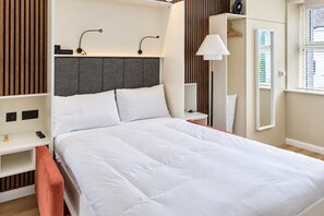 Un lit bien fait dans une chambre d’hôtel, avec une tête de lit, des tables de chevet, une lampe et une armoire.
