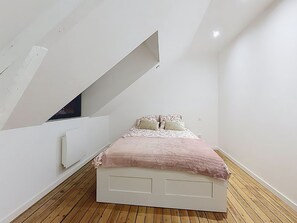 A bedroom with a sloped ceiling, a bed with a pink blanket, and wooden flooring. - La Maison du Port – Beach within walking distance, peaceful and comfortable (Dives-sur-Mer)