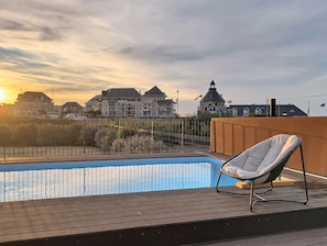 Ein Swimmingpool mit Liege, umgeben von einer Holzterrasse und einem Zaun.