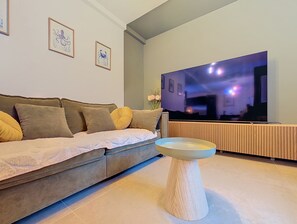 A living room with a sofa, a coffee table, and a flat-screen TV mounted on the wall. - La Maison du Port – Beach within walking distance, peaceful and comfortable (Dives-sur-Mer)