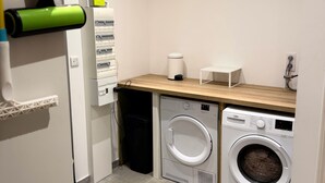 A laundry room with a washing machine, dryer, and a small trash bin. - La Maison du Port – Beach within walking distance, peaceful and comfortable (Dives-sur-Mer)