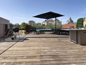 Eine Dachterrasse mit Grill, Liegestühlen, einem Billardtisch und einem großen Sonnenschirm.
