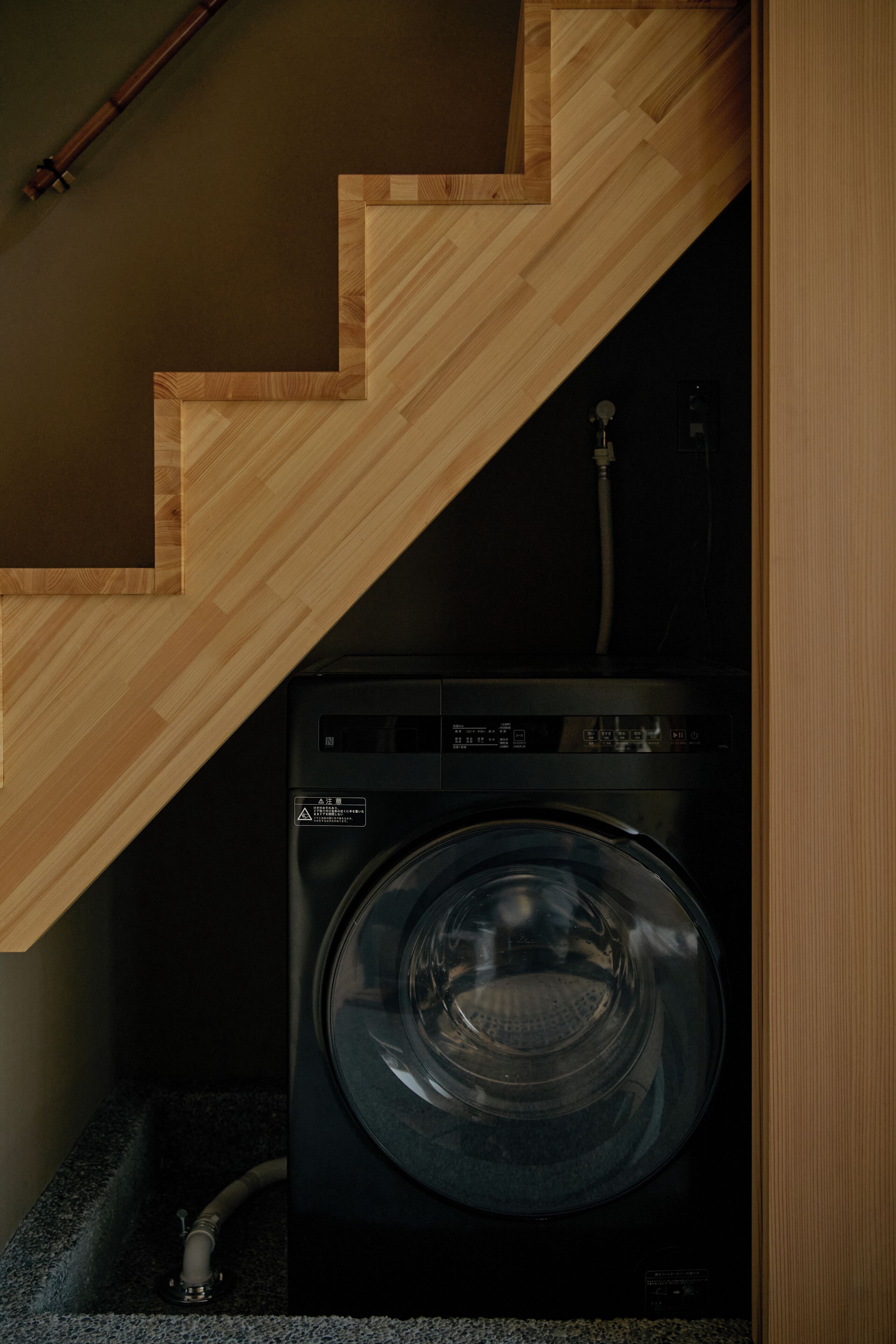 A washing machine under a wooden staircase in a laundry room.
