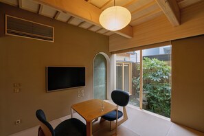 A room with a wooden ceiling, a flat-screen TV mounted on the wall, a small table with chairs, and a large window with a view of greenery outside. - NEW | Private Kyoto Machiya | Walking Distance to Gion & Shirakawa (京都市京都市東山区北木之元町)
