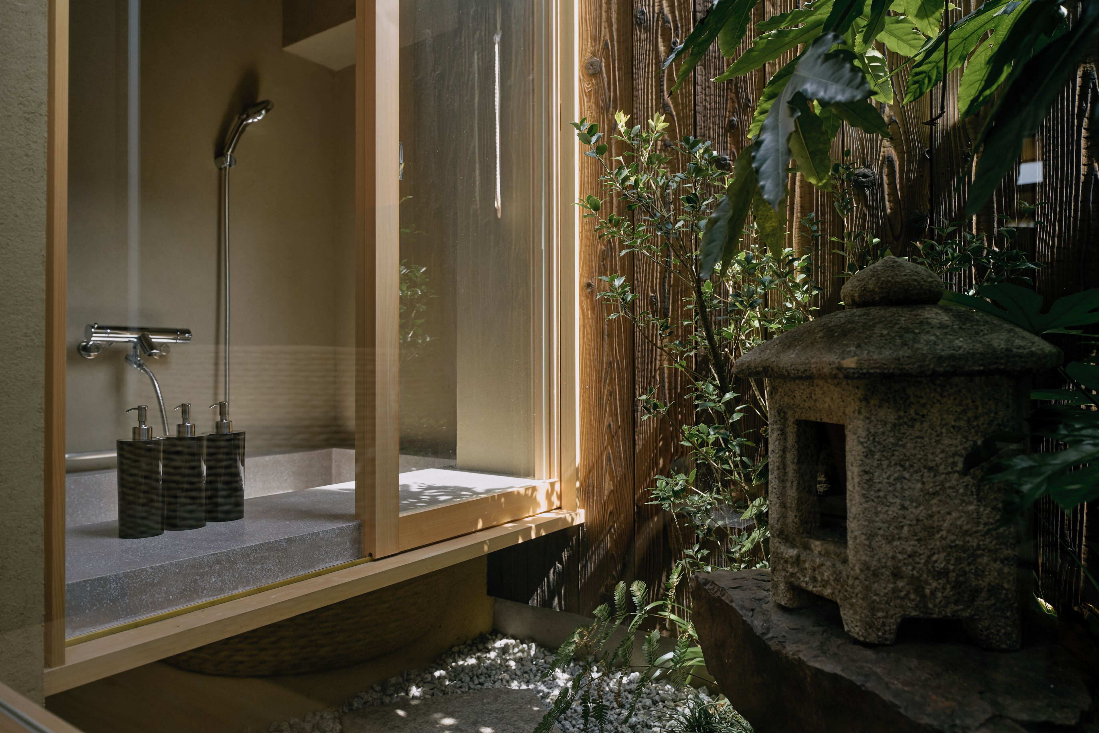 A bathroom with a shower, a sink with soap dispensers, and a stone lantern.