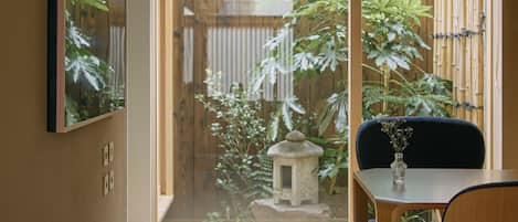 A room with a sliding glass door leading to a garden, a dining table with chairs, and a framed picture on the wall.