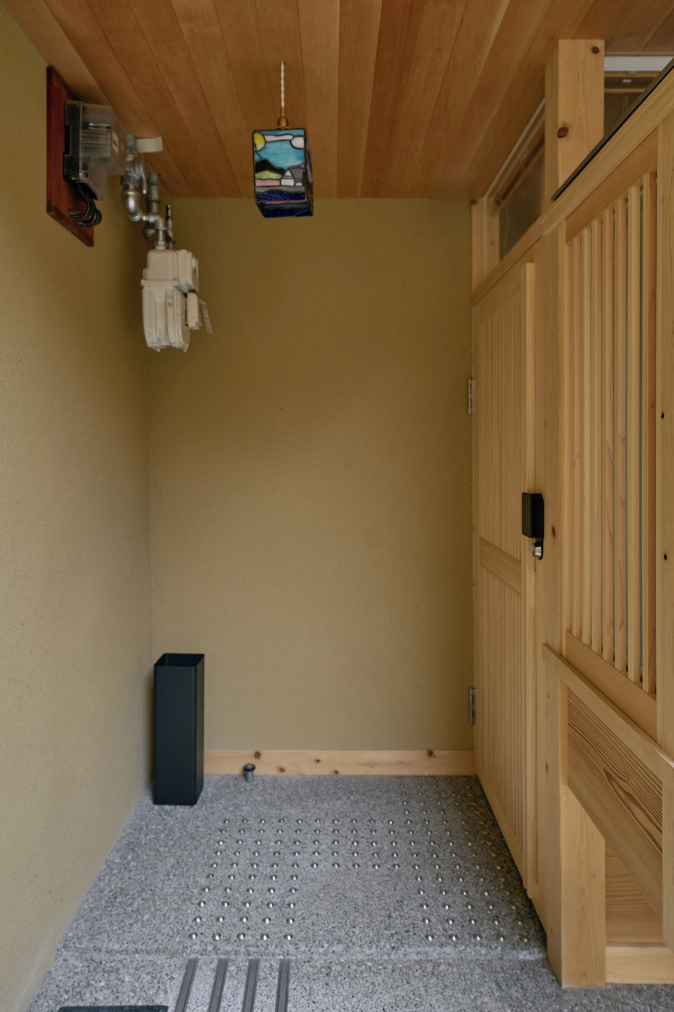 Ein Zimmer mit Holzbalkendecke, einem kleinen Wandheizgerät, einer Holztür und einem strukturierten Boden.