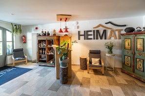 Een hotellobby met een houten kast, een boekenkast, een zithoek en een muur waarop 'HEIMAT' staat.