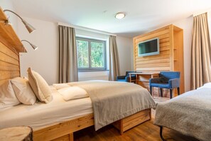 Een kamer met twee bedden, een bureau, een stoel, een televisie en een raam met gordijnen.