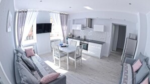 A modern kitchen with white cabinets, a stainless steel range hood, and a dining area with a table and chairs.